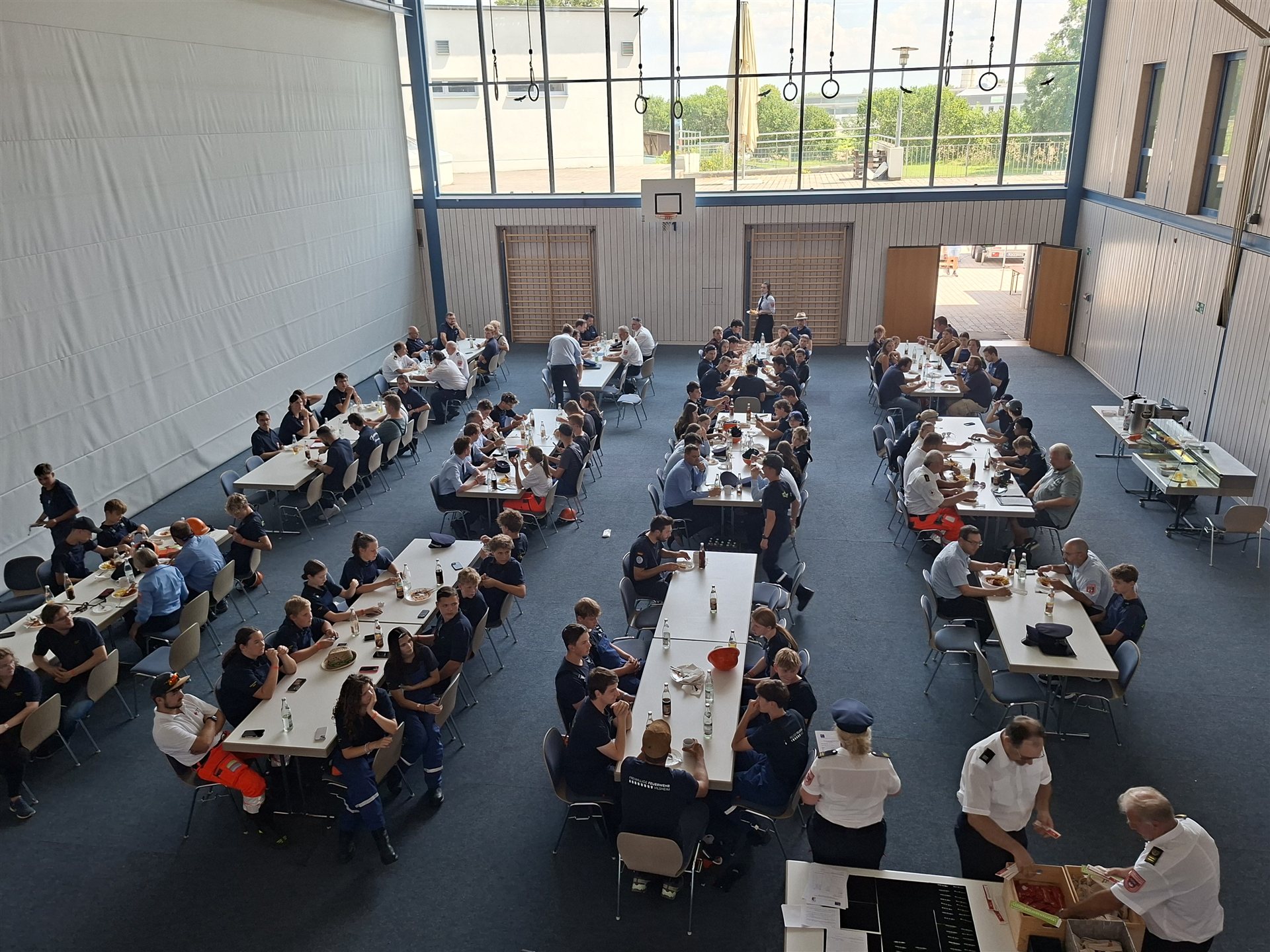Die Teilnehmerinnen und Teilnehmer an langen Tischreihen in der Halle